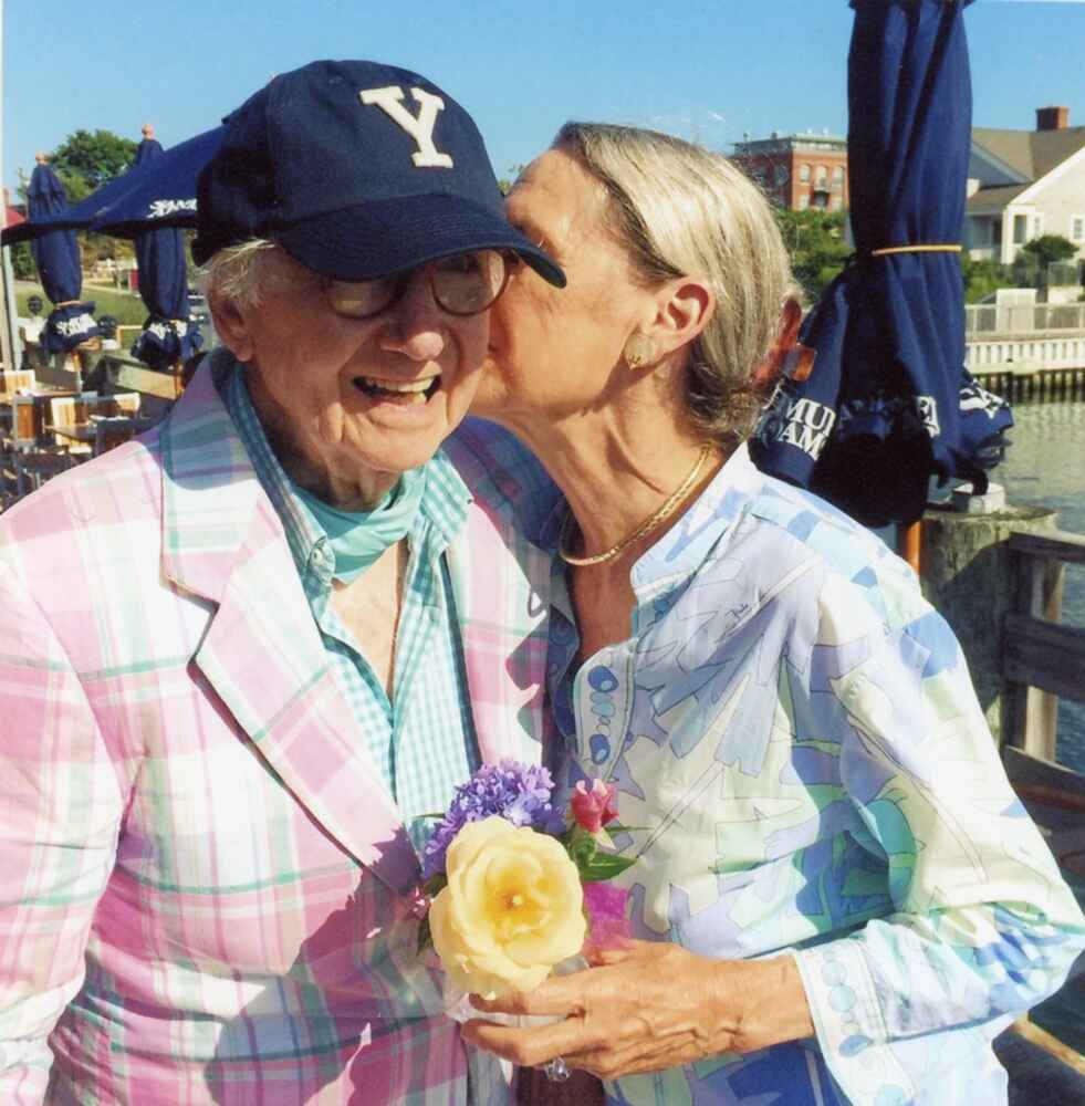 Alexandra kissing Peter on the cheek while holding a bouquet of flowers.